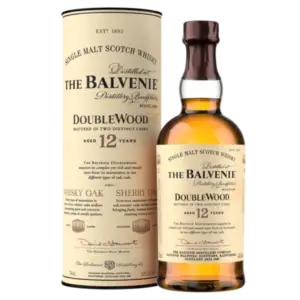 בקבוק של The Balvenie DoubleWood 12 Year Old Single Malt Scotch Whisky עומד ליד המארז הגלילי התואם שלו, שניהם עם תוויות בצבע שמנת עם טקסט שחור וזהב.