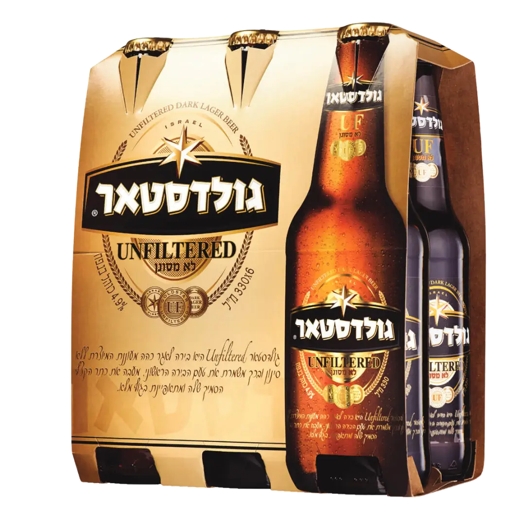 שישיית גולדסטאר לא מסוננת, בירה כהה בבקבוקים חומים עם תוויות זהב ושחור, נראית חלקית בתוך קרטון זהוב וחום עם טקסט בעברית ובאנגלית.